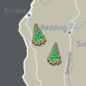 May include: A map of California with two green and gold tree-shaped pins near Redding. The word "Eureka" is visible at the top left, and "Sacramento" is written vertically on the right side of the map.