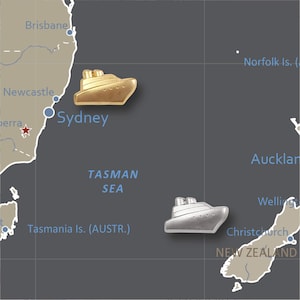 May include: A map of Australia and New Zealand with a gold and silver cruise ship pin on Sydney and Auckland, respectively. The map shows the Tasman Sea between the two countries.