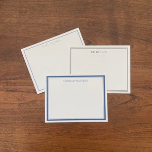 May include: Three white note cards with blue and black borders. The top card has the text "LUKE SACHSEL" printed in black. The middle card has the text "ED DOERR" printed in black. The bottom card has the text "CONRAD WALTERS" printed in black.