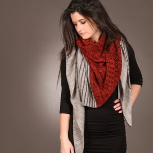 Peut inclure: Une femme porte une écharpe ajourée de couleur rouille et un châle à motifs gris et noirs. L'écharpe est drapée sur une robe noire. Le châle a un motif rayé. Le fond est de couleur neutre unie.