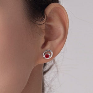 Puede incluir: Un par de pendientes de plata con una piedra preciosa roja engastada en un círculo.