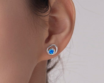 May include: A pair of silver stud earrings with a blue opal stone set in a circle.