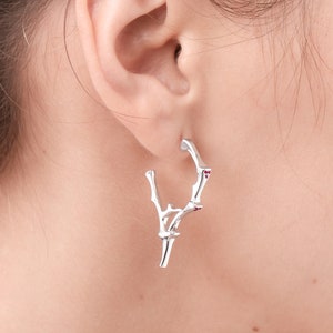 May include: Silver hoop earrings with a branch design and small red gemstones.