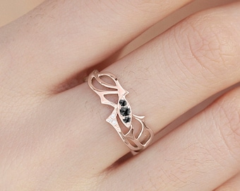 May include: A delicate rose gold ring with a unique, intricate design featuring black diamonds. The ring is shown on a finger.