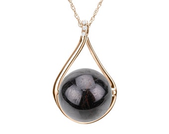 May include: A gold-toned pendant necklace featuring a teardrop-shaped frame. The frame holds a dark, spherical stone. The necklace chain is delicate, and small, clear stones accent the top of the pendant.