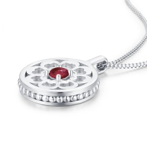 以下が含まれることがあります： 繊細な花のデザインと中央に赤い宝石をあしらった丸いペンダントが付いたシルバーネックレスです。