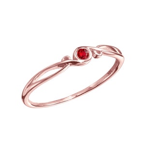 May include: A delicate rose gold ring featuring a single red gemstone set in a simple, elegant design.