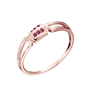 May include: A rose gold ring with a delicate design featuring a row of small red gemstones.