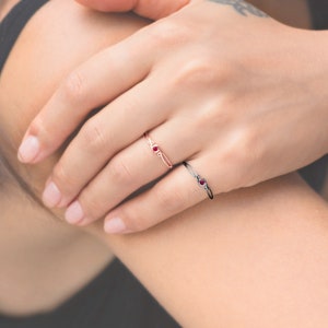 May include: Two delicate rings with red gemstones. The ring on the left is a thin band with a single red gemstone. The ring on the right is a thicker band with a single red gemstone and a small diamond on each side.