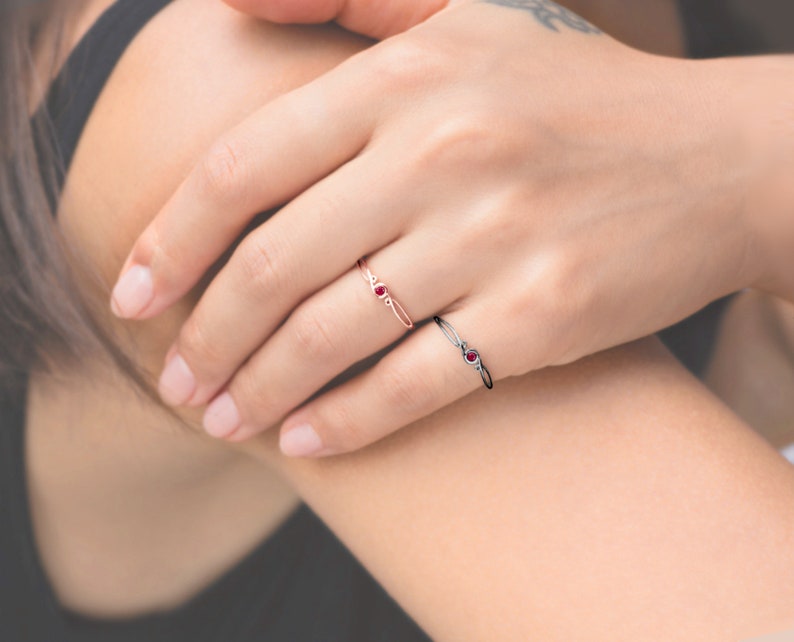 May include: Two delicate rings with red gemstones. The ring on the left is a thin band with a single red gemstone. The ring on the right is a thicker band with a single red gemstone and a small diamond on each side.
