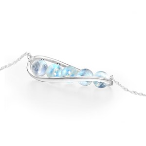 May include: A silver necklace with a curved pendant featuring a row of iridescent blue moonstone beads.