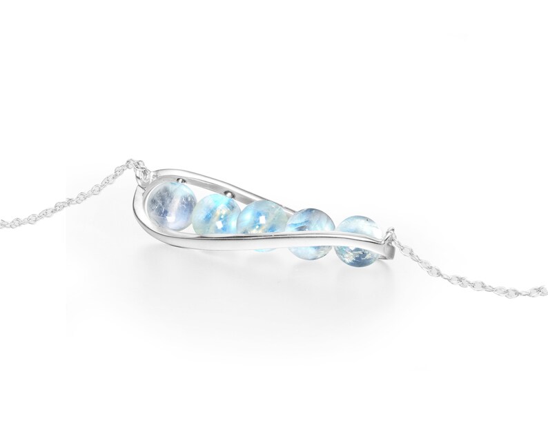 May include: A silver necklace with a curved pendant featuring a row of iridescent blue moonstone beads.
