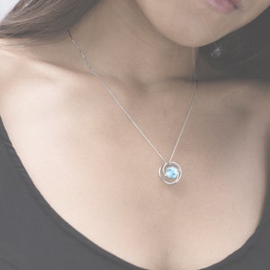 May include: A silver chain necklace with a delicate pendant featuring a light blue gemstone surrounded by two silver rings.