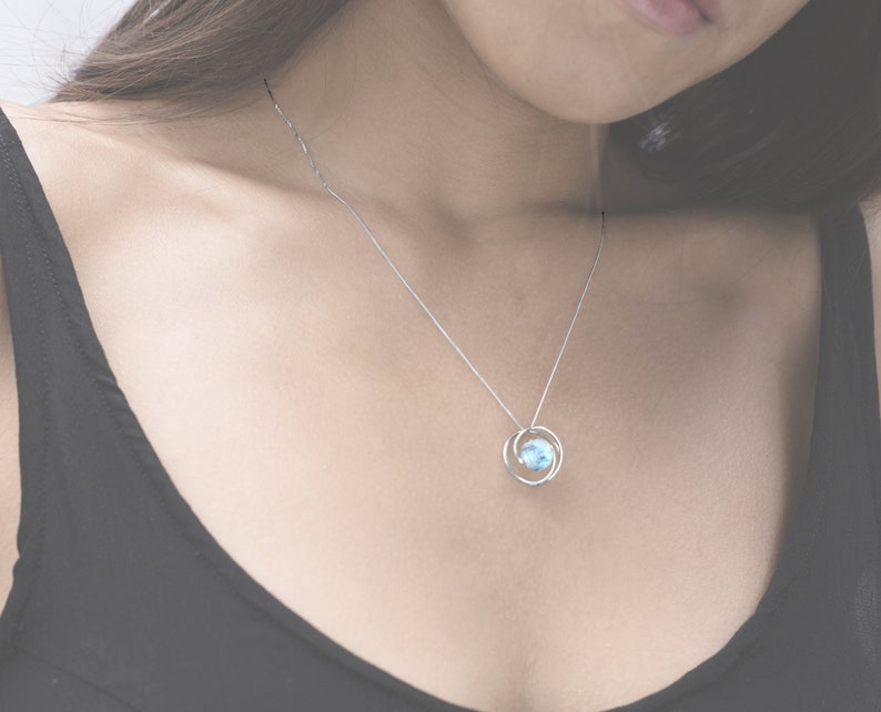 May include: A silver chain necklace with a delicate pendant featuring a light blue gemstone surrounded by two silver rings.