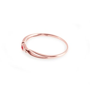 May include: A delicate rose gold ring with two small red gemstones. The ring is marked "14K" on the inside.