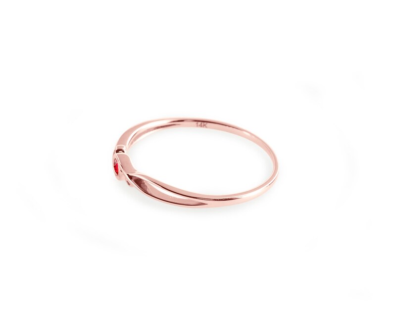 May include: A delicate rose gold ring with two small red gemstones. The ring is marked "14K" on the inside.