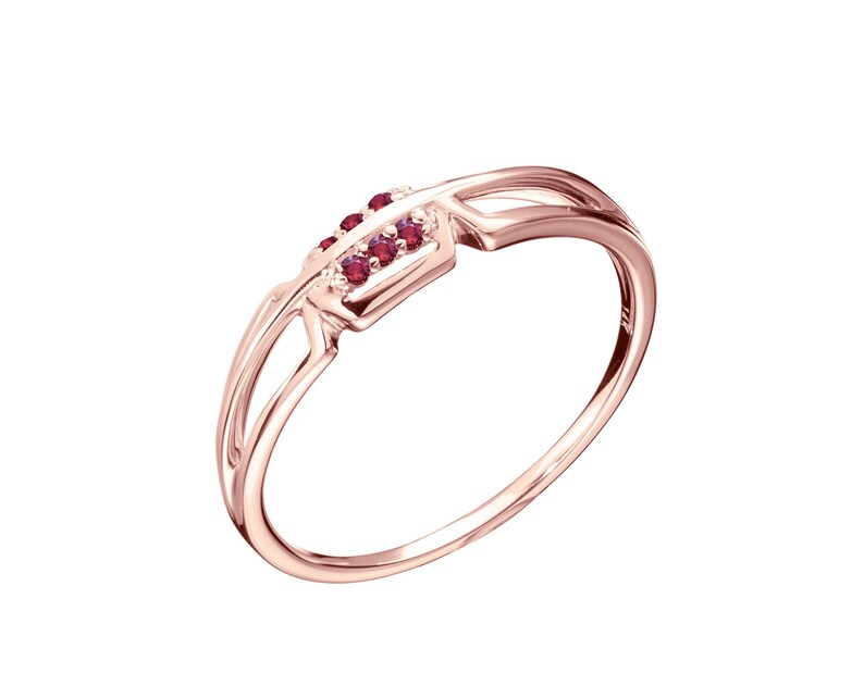 May include: A rose gold ring with a delicate design featuring a row of small red gemstones.