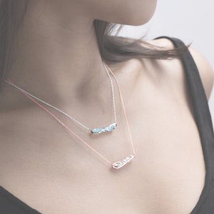 May include: Two delicate necklaces with silver chains and small charms. The top necklace features a row of light blue stones, while the bottom necklace has a single charm shaped like a pea pod.