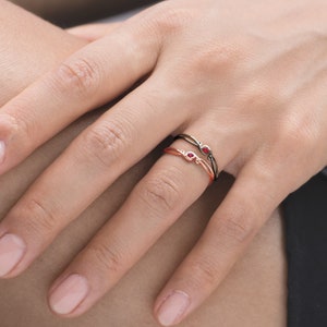 May include: Two delicate rings with red gemstones. The rings are intertwined and feature a simple, elegant design.