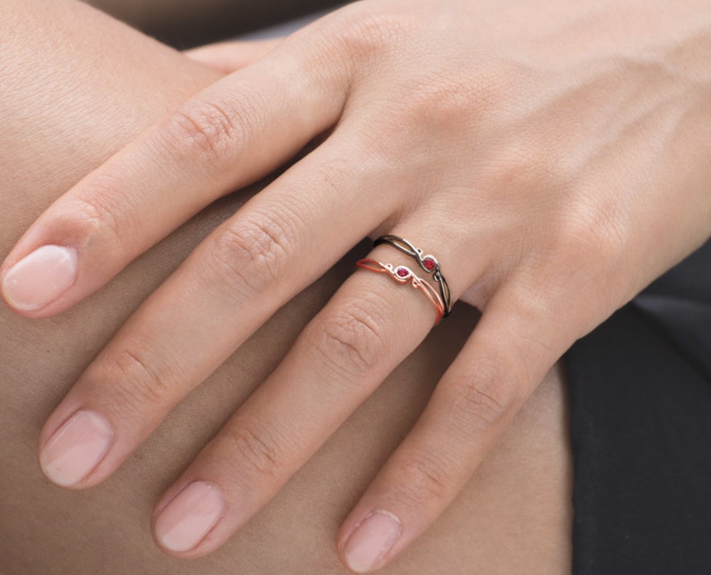 May include: Two delicate rings with red gemstones. The rings are intertwined and feature a simple, elegant design.