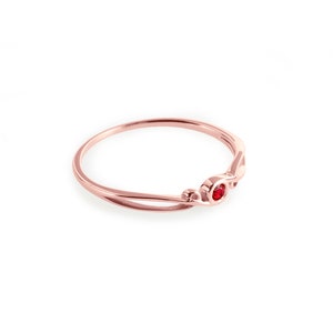 May include: A delicate rose gold ring with a single red gemstone set in the centre.