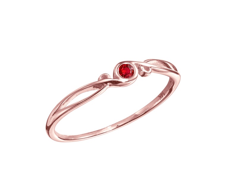 May include: A delicate rose gold ring featuring a single red gemstone set in a simple, elegant design.