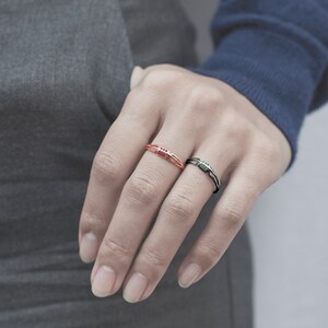 May include: Two thin rings with small stones. The ring on the left has red stones and the ring on the right has green stones.