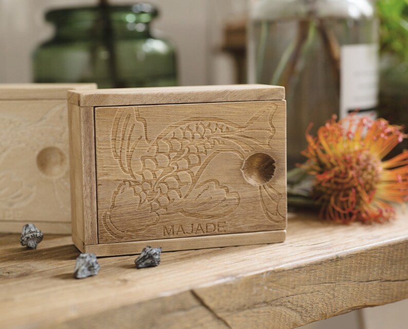 May include: A wooden box with a carved fish design and the word "MAJADE" on the front. The box is open and has a small compartment inside.