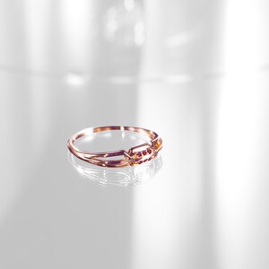 May include: A gold ring with a delicate design and small red gemstones. The ring is on a white surface.