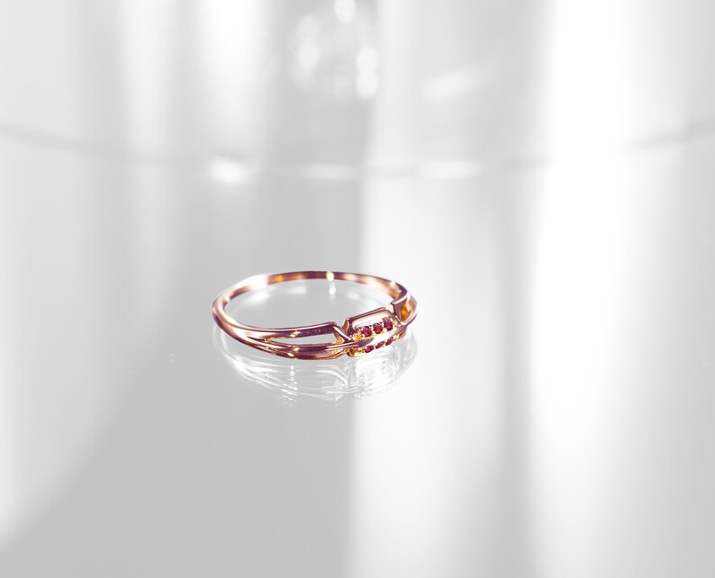 May include: A gold ring with a delicate design and small red gemstones. The ring is on a white surface.