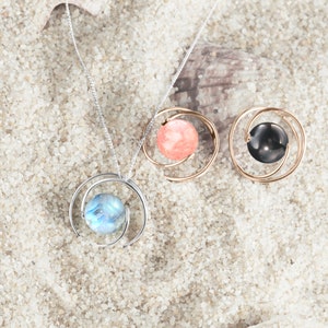 May include: Three silver necklaces with different colored stones in a swirling design. The stones are pink, blue, and black.