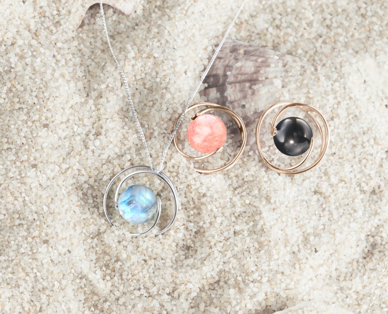 May include: Three silver necklaces with different colored stones in a swirling design. The stones are pink, blue, and black.