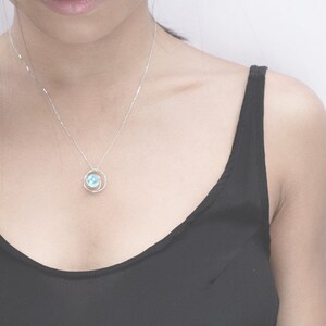 May include: A silver necklace with a delicate pendant featuring a light blue gemstone surrounded by a silver circle.