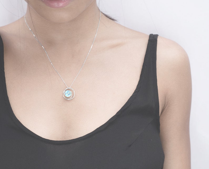 May include: A silver necklace with a delicate pendant featuring a light blue gemstone surrounded by a silver circle.