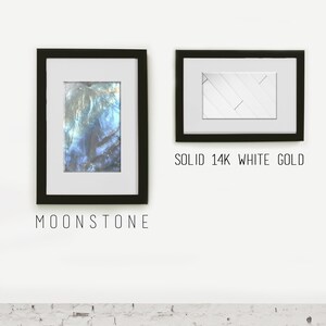 May include: Two framed images on a white wall. The image on the left is a close-up of a blue and green iridescent gemstone with the text "MOONSTONE" below. The image on the right is a white geometric pattern with the text "SOLID 14K WHITE GOLD" below.