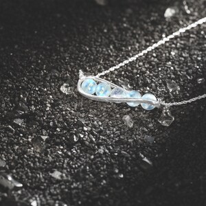 May include: A silver necklace with a delicate chain and a pendant shaped like a pod with five light blue gemstones.