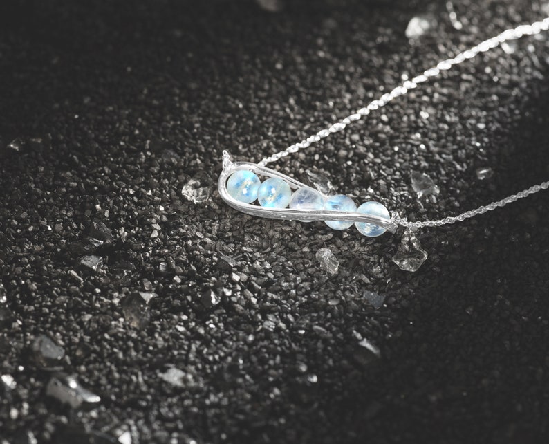 May include: A silver necklace with a delicate chain and a pendant shaped like a pod with five light blue gemstones.
