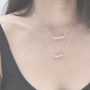 May include: Two delicate necklaces with a silver chain and a thin rose gold chain. The silver chain has a blue gemstone pendant and the rose gold chain has a white gemstone pendant.