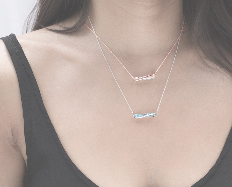 May include: Two delicate necklaces with a silver chain and a thin rose gold chain. The silver chain has a blue gemstone pendant and the rose gold chain has a white gemstone pendant.