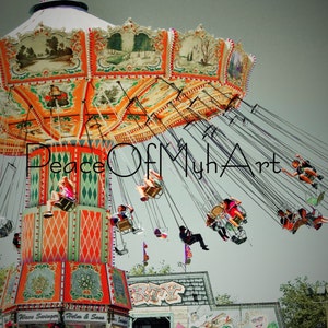 May include: A vintage-style carnival ride with colorful, painted details. The ride is a swing set with multiple seats hanging from chains. The seats are filled with people enjoying the ride. The ride is set against a light gray sky.