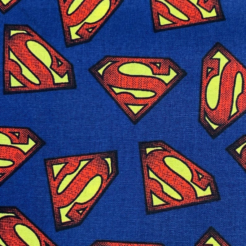Pu&ograve; includere: Un tessuto blu con un motivo ripetuto di loghi Superman rossi e gialli.
