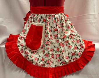 May include: A red and white floral apron with a ruffled hem and a large red pocket. The apron has a white background with a pink and green floral pattern.