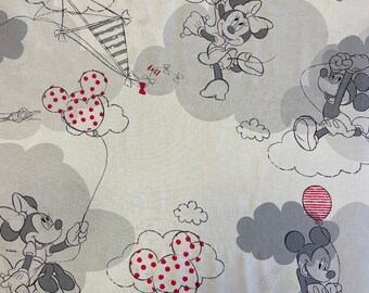 Op de afbeelding: Een witte stof met een herhalend patroon van Mickey Mouse en Minnie Mouse-figuren. De figuren zijn in zwart-wit getekend en houden rode en witte ballonnen vast. De achtergrond is lichtgrijs met wolken.