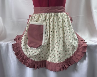 May include: A pink and white floral print apron with a large pink pocket and a ruffled hem.