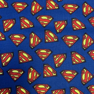 Pu&ograve; includere: Un tessuto blu con un motivo ripetuto di loghi Superman rossi. I loghi sono contornati di giallo e hanno un aspetto testurizzato.
