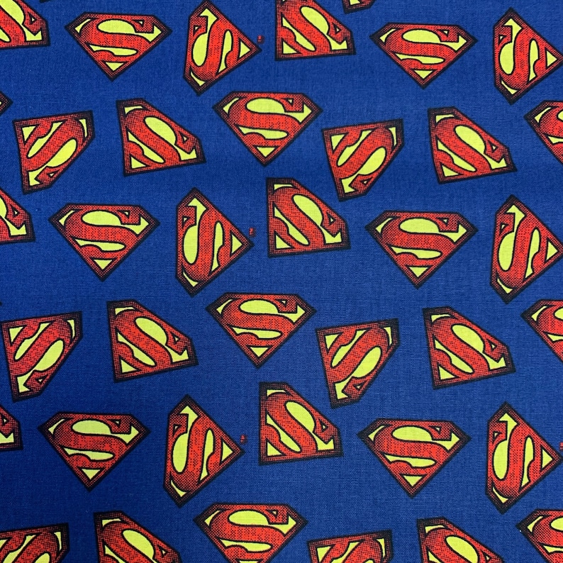 Pu&ograve; includere: Un tessuto blu con un motivo ripetuto di loghi Superman rossi. I loghi sono contornati di giallo e hanno un aspetto testurizzato.