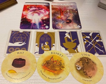 May include: A collection of tarot cards featuring various illustrations and text. The cards are arranged on a white surface, with some cards stacked in the background. The cards include images of a hat, basket, and lion.