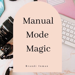 May include: A pink composition book with the text "COMPOSITION BOOK" on the cover, a camera lens, a camera body, and a white keyboard with the text "Manual Mode Magic" and "Brandi Inman" on a light pink background.