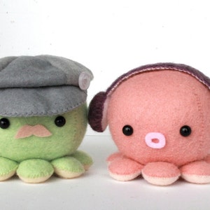 Op de afbeelding: Twee pluche octopus speelgoedjes. Eén is groen met een grijze hoed en een snor. De andere is roze met paarse koptelefoons.