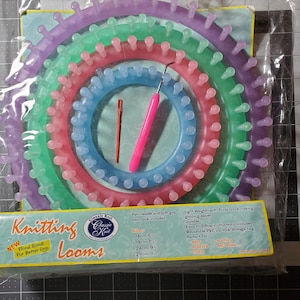May include: A set of colorful knitting looms in a clear plastic bag. The looms are in shades of purple, green, pink, and blue. Included are a pink crochet hook and a red yarn needle. The packaging reads "Knitting Looms".